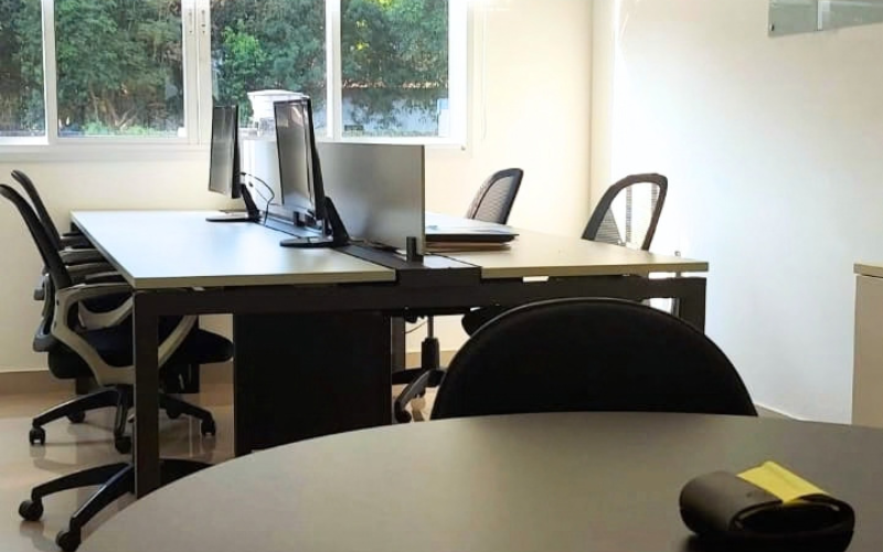 Sala privativa Esmeralda do Trampô Space, mesa com monitores e vista para árvores.